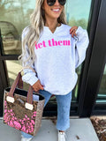 Woman wearing a white sweatshirt with pink text, holding a floral handbag, standing outside.