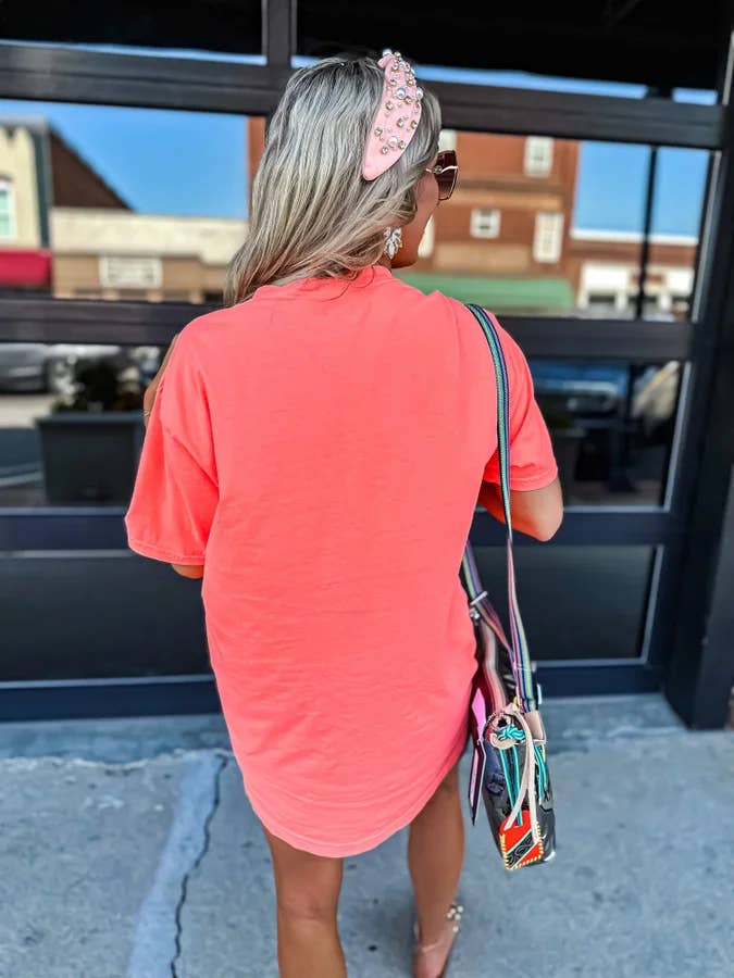 Woman in a coral dress with a headband and sunglasses, walking past a store entrance.