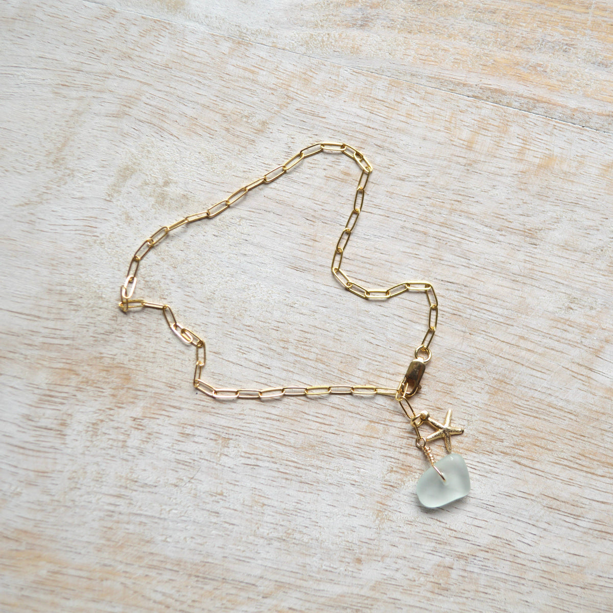 Gold chain necklace with a star and clear stone pendant on a wooden surface