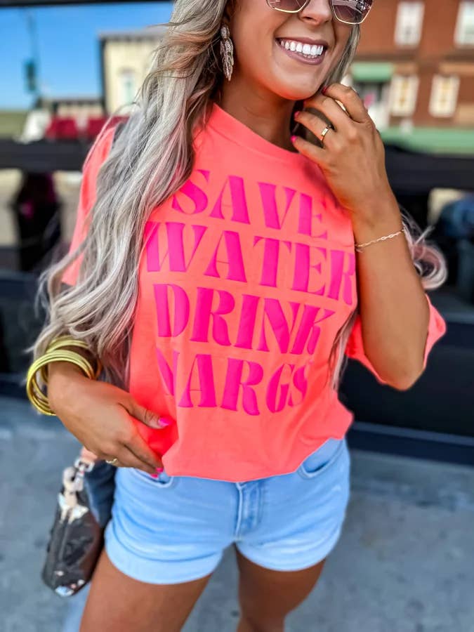 Person wearing a bright pink 'SAVE WATER DRINK WARGS' shirt outdoors.