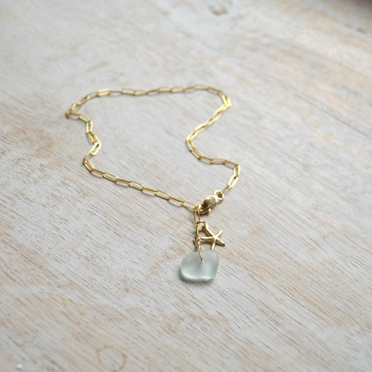Gold chain necklace with a heart-shaped pendant on a light wooden surface