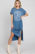 A woman modeling a blue acid-wash denim t-shirt dress with a distressed white cowgirl graphic on the front. The dress features a high-low asymmetrical hem and side slit, styled with cream-colored cowboy boots against a light gray studio background.