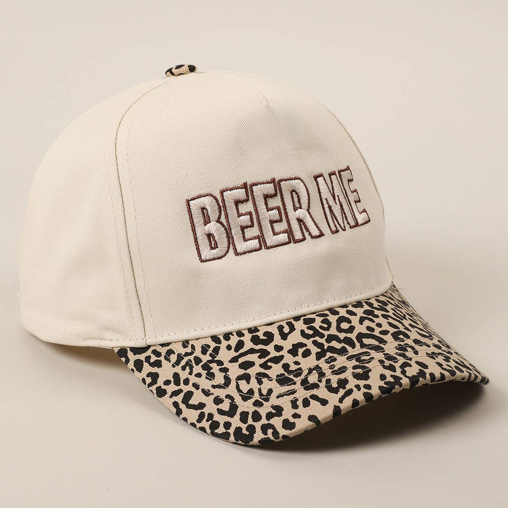 An off-white baseball cap with 'BEER ME' embroidered on the front in brown outlined letters, featuring a leopard-print patterned visor.