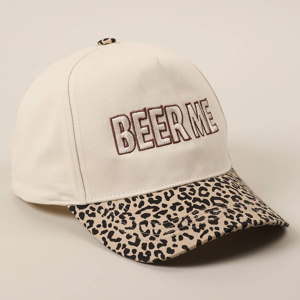 An off-white baseball cap with 'BEER ME' embroidered on the front in brown outlined letters, featuring a leopard-print patterned visor.