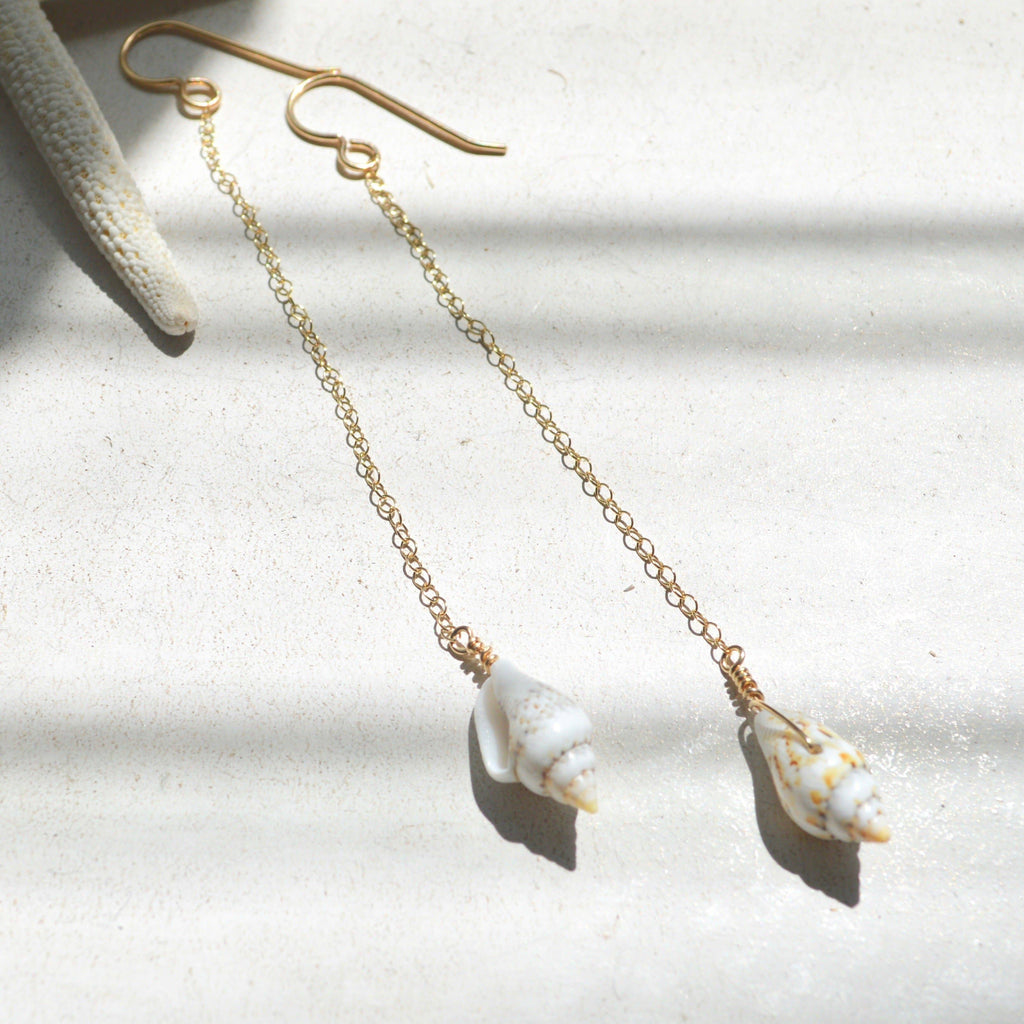 Gold chain earrings with shell pendants on a light background