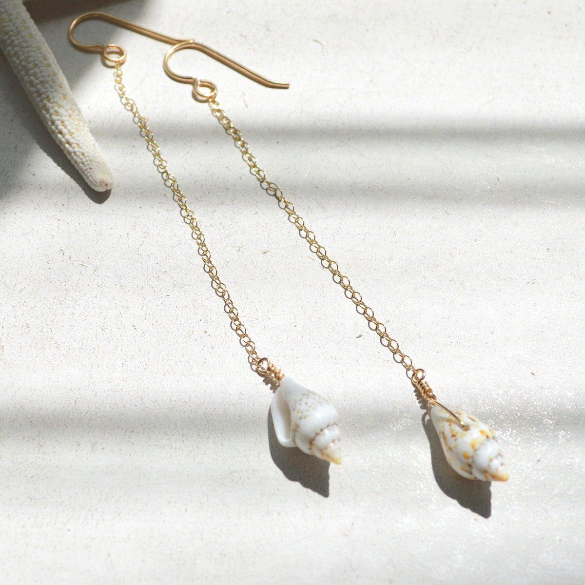 Gold chain earrings with shell pendants on a light background