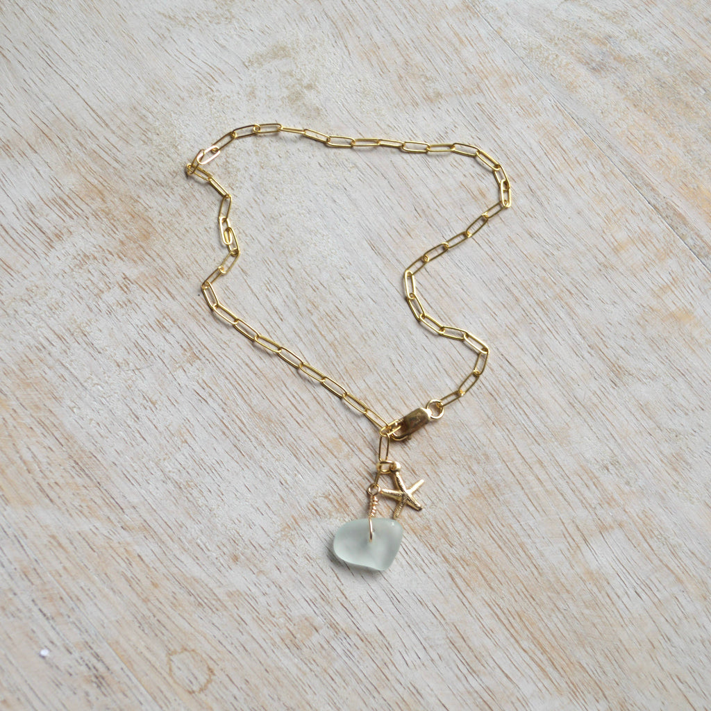 Gold chain necklace with a light blue pendant on a wooden surface