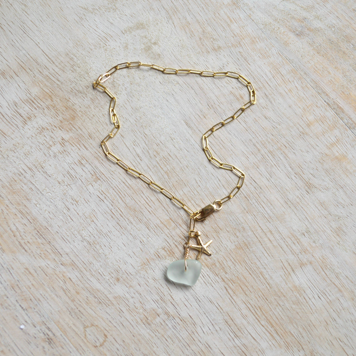 Gold chain necklace with a light blue pendant on a wooden surface