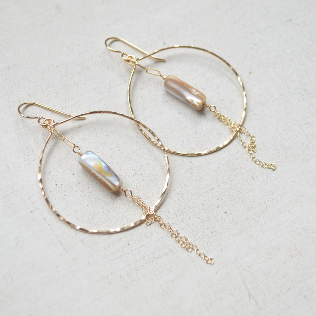 Gold hoop earrings with pearl-like beads on a light gray background