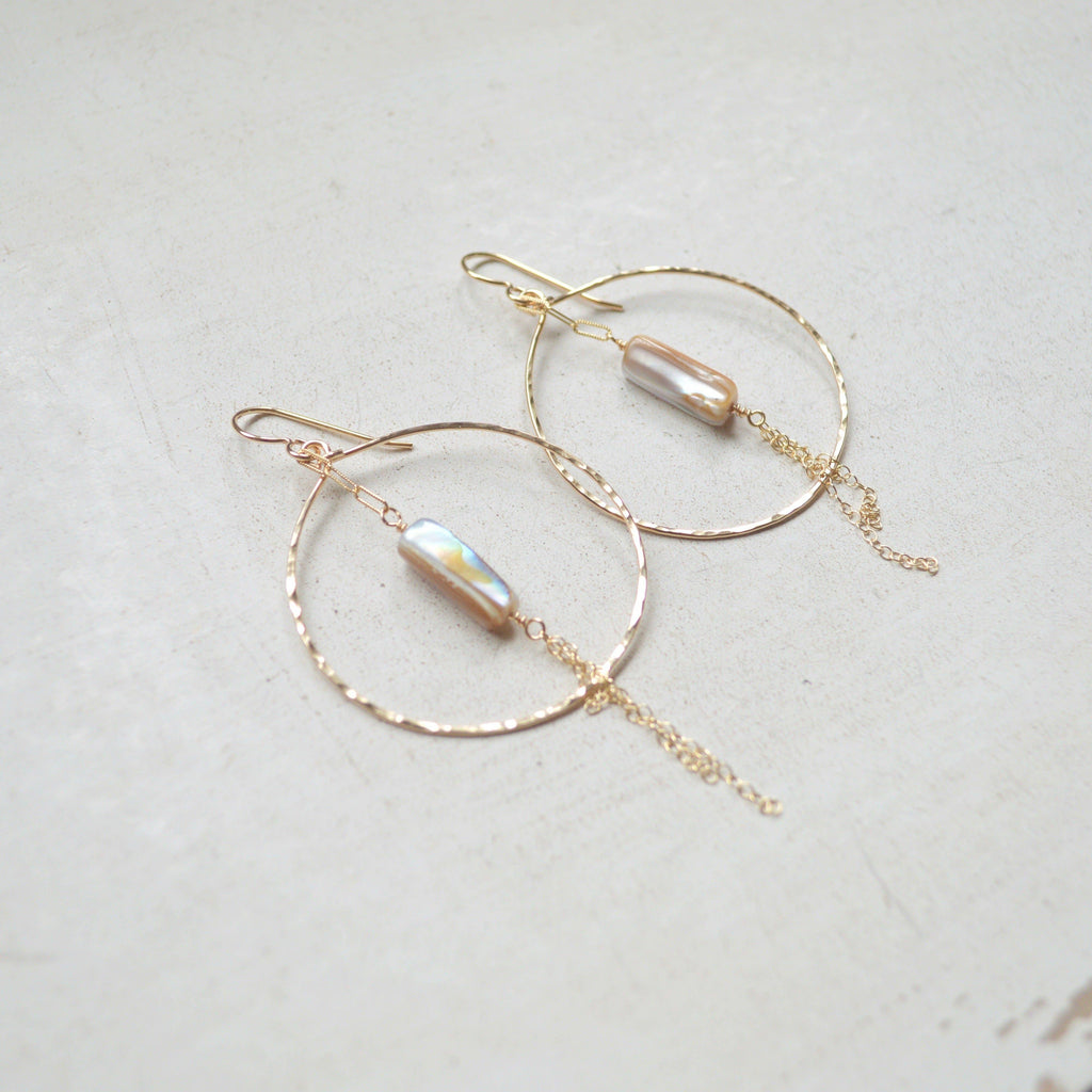Gold hoop earrings with pearl-like beads on a light gray background
