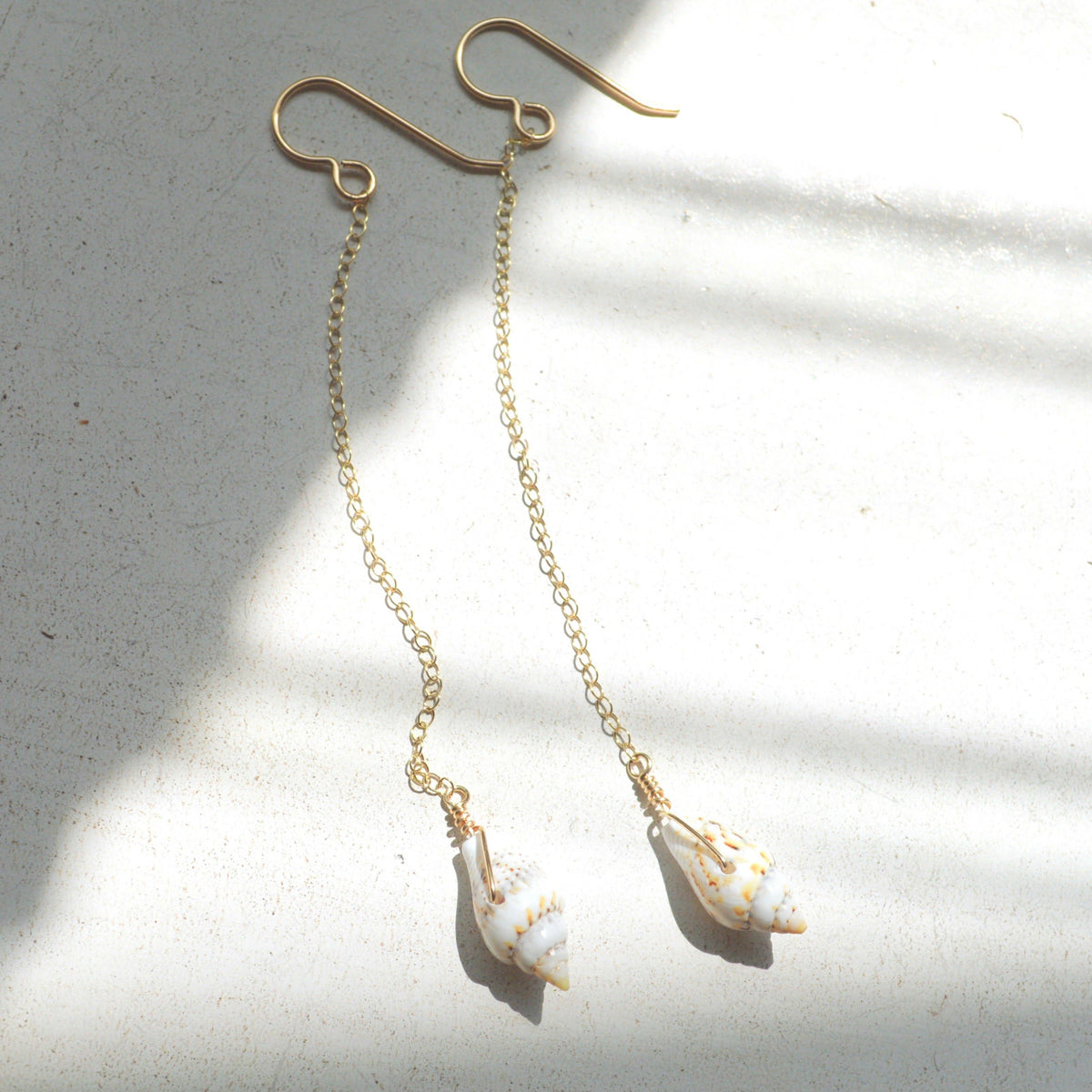 Shell-shaped earrings on gold chains against a light background