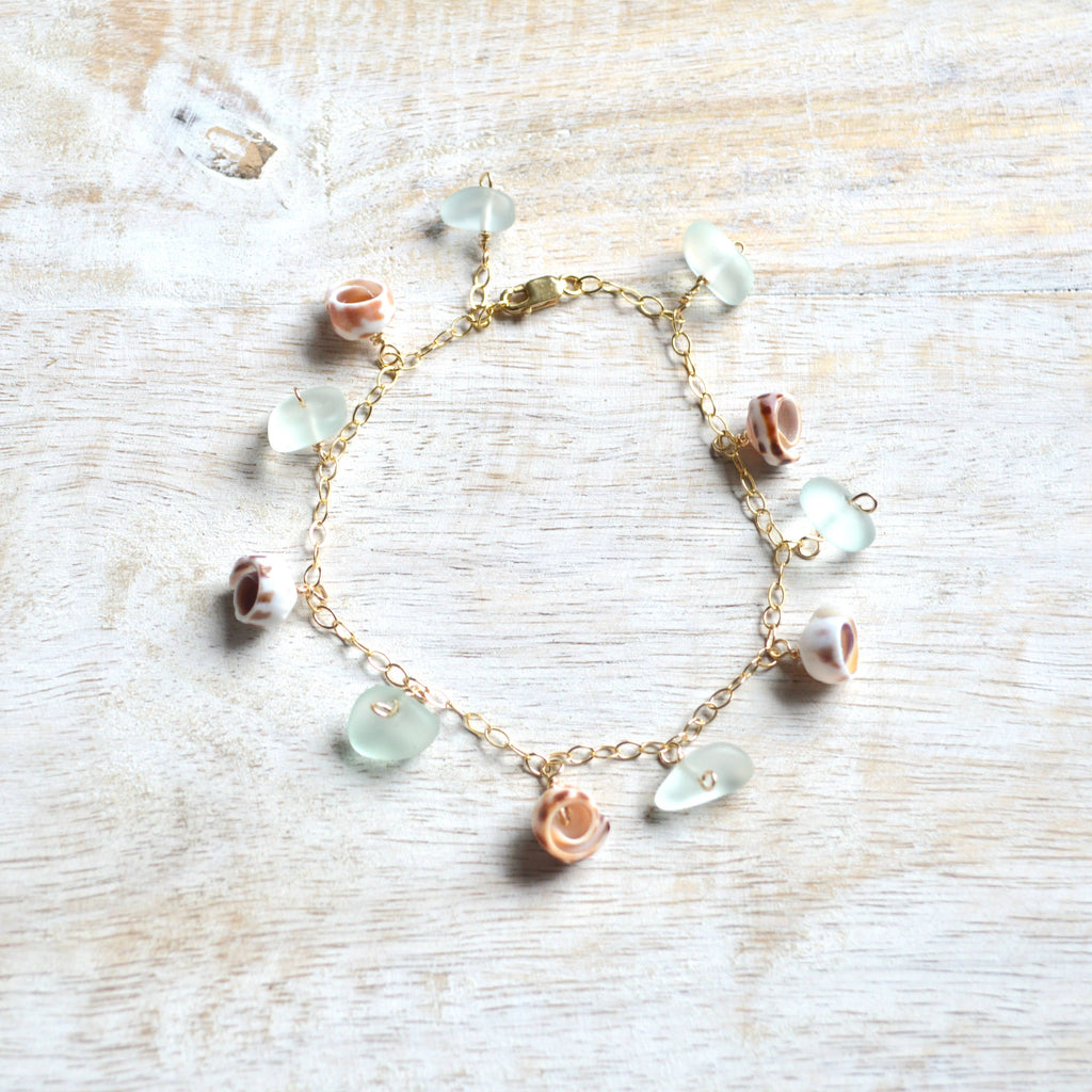 Bracelet with sea glass and shell charms on a light wooden surface