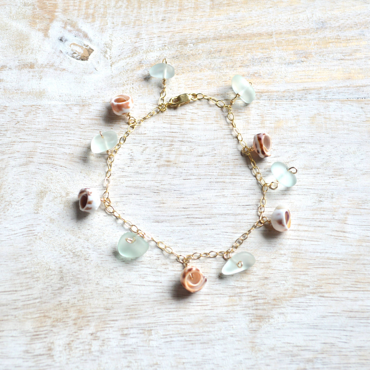 Bracelet with sea glass and shell charms on a light wooden surface