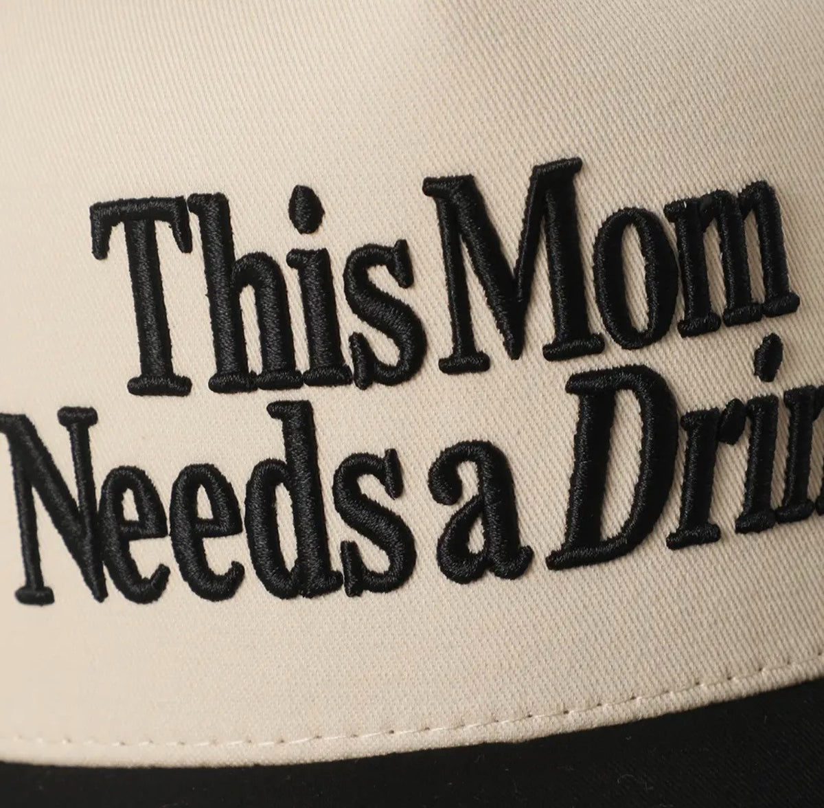 Beige cap with black text 'This Mom Needs a Drink' on a beige background
