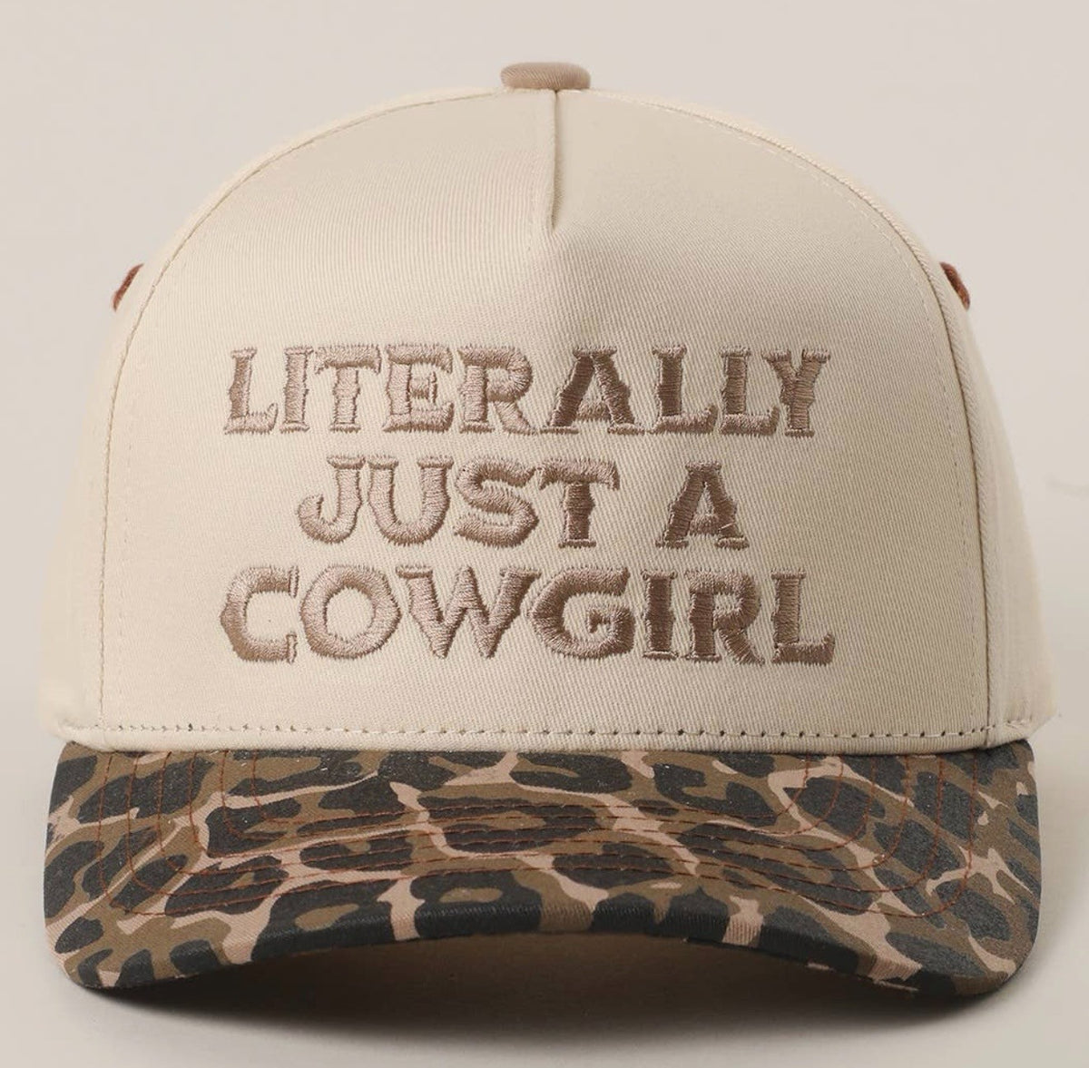 A beige snapback cap with brown embroidered text reading 'LITERALLY JUST A COWGIRL' on the front, featuring a leopard-print patterned visor.
